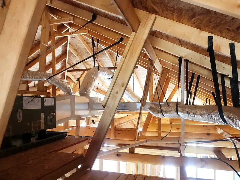 Insulated flex duct runs strapped to the rafters in an attic, leading away from a new air handler