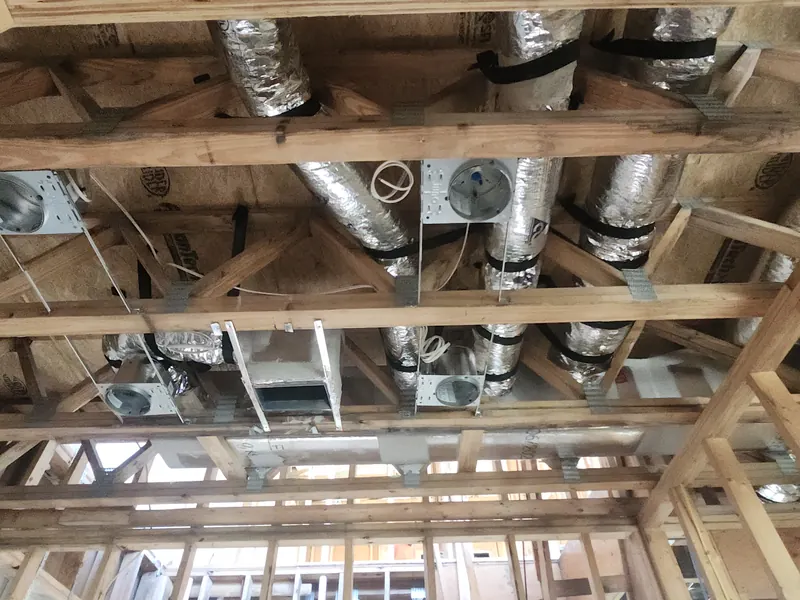 Insulated duct runs connected to ceiling supply boots between joists in a new home