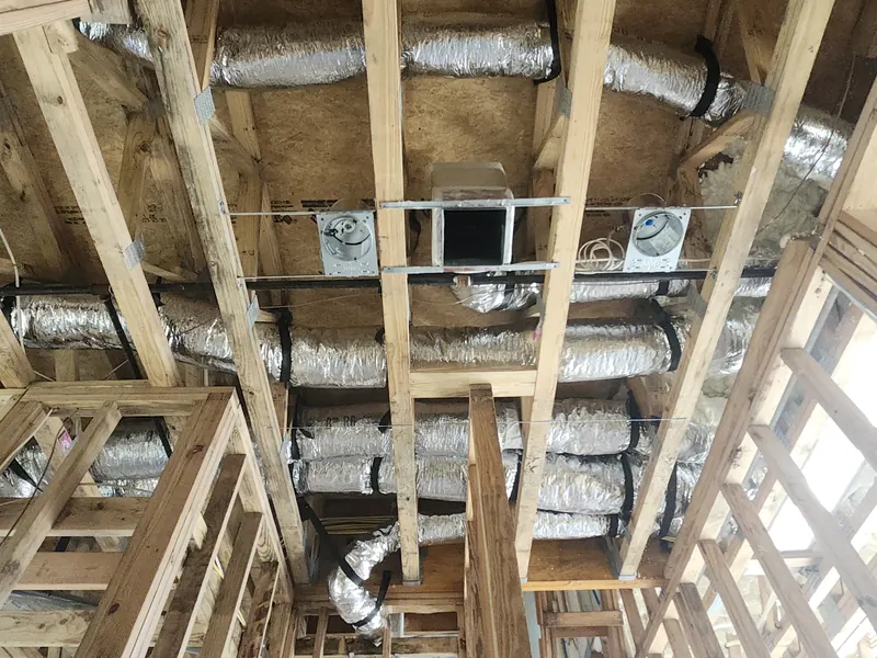 Rows of insulated supply ducts running between ceiling joists in a new home before drywall