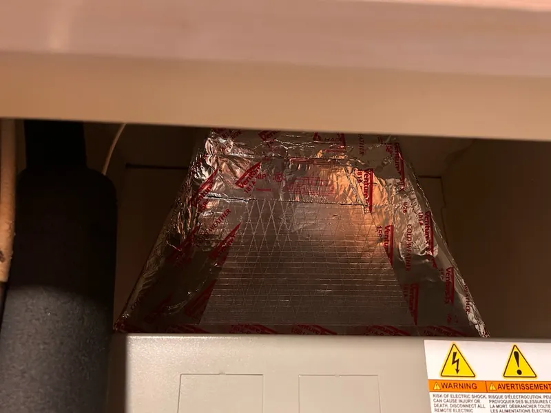 Foil-faced insulated supply plenum sitting on top of an air handler in a closet